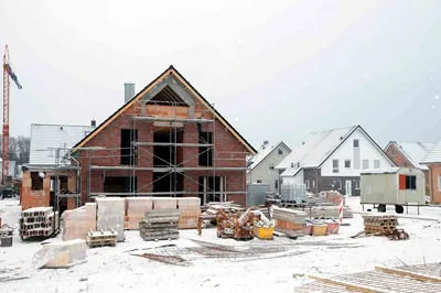 Backsteinhaus im Rohbau in einer Neubausiedlung, Schnee auf den Dächern